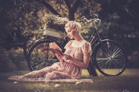 树下草地上的看书美女和自行车图片