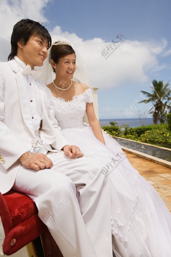 穿着洁白婚纱礼服的男女坐在海边远望图片图片