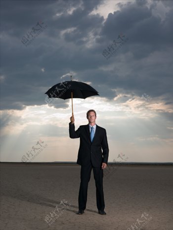 阴天打伞站在沙漠里的外国商业男人图片