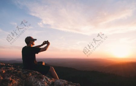 夕阳下悬崖上拍照的男人